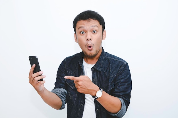 Giovane uomo asiatico scioccato quando guarda e indica lo smartphone