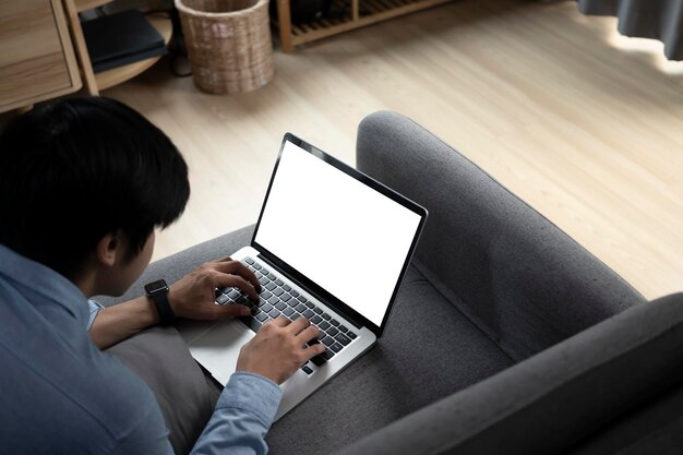 Giovane uomo asiatico sdraiato sul divano e navigare in internet con il computer portatile