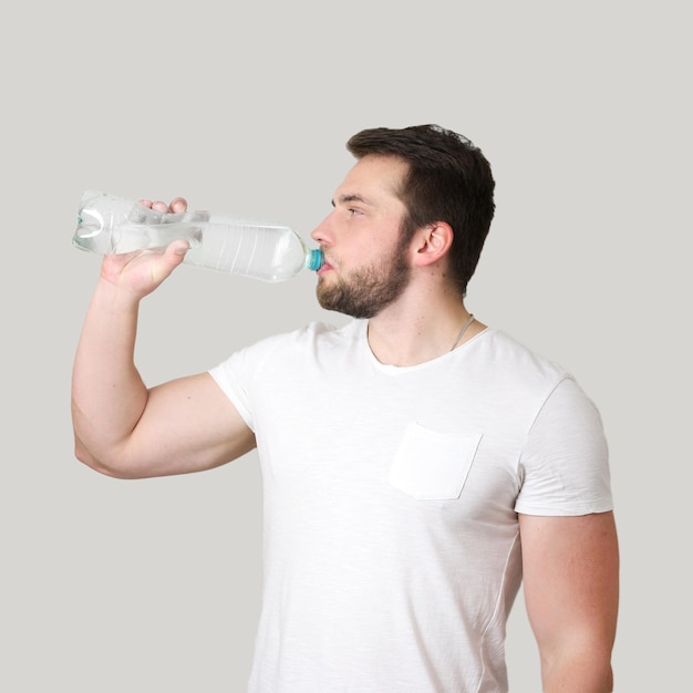 Giovane uomo atletico acqua potabile da una bottiglia su sfondo isolato