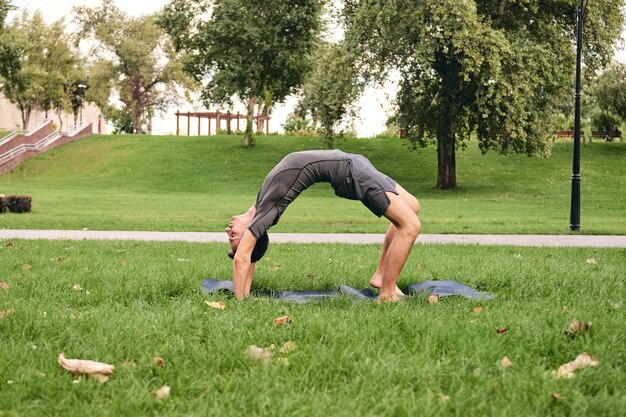 Giovane uomo atletico in abiti sportivi che fa yoga nel parco