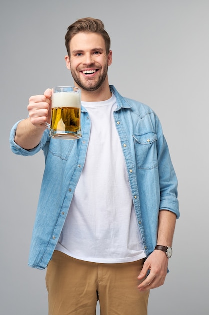 Giovane uomo azienda indossa jeans shirt tenendo un bicchiere di birra in piedi