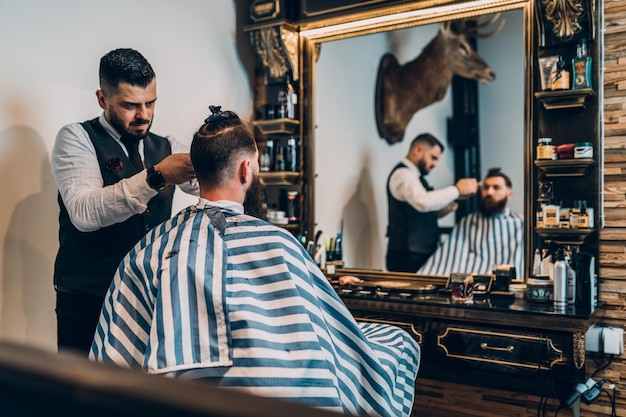 Giovane uomo barbuto bello hipster che visita parrucchiere nel negozio di barbiere.