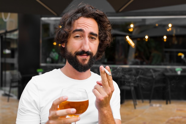 Giovane uomo barbuto che fuma e che beve una birra