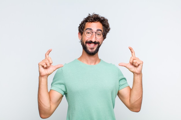 Giovane uomo barbuto che incornicia o delinea il proprio sorriso con entrambe le mani, guardando positivo e felice, concetto di benessere