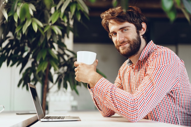 Giovane uomo barbuto che indossa una camicia casual utilizzando il suo computer portatile. Ritratto di uomo d'affari