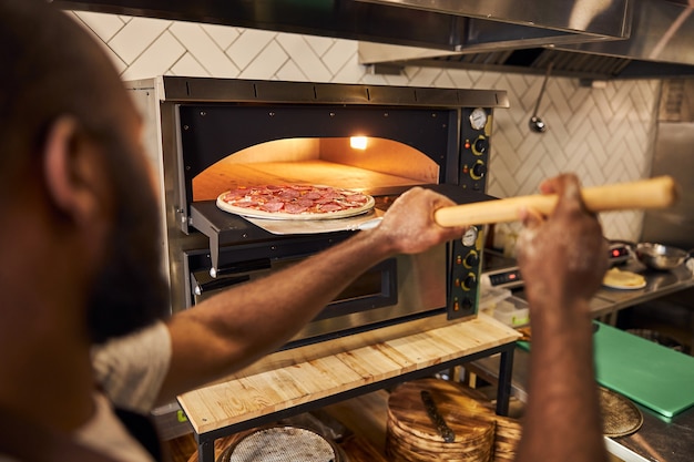 giovane uomo barbuto che lavora in cucina e mette il piatto nel forno professionale per la cottura