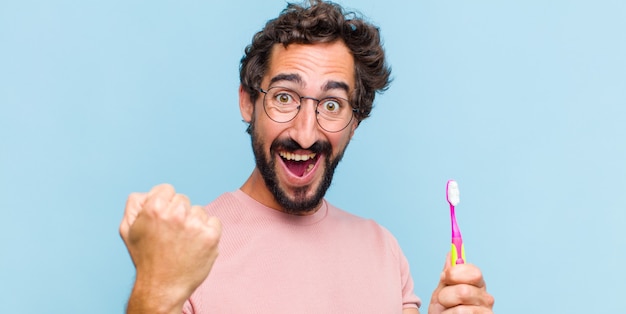 Giovane uomo barbuto che si sente felice, positivo e di successo, celebra la vittoria, i risultati o la buona fortuna