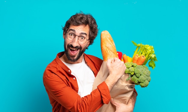 Giovane uomo barbuto che si sente felice, positivo e di successo, motivato quando affronta una sfida o celebra buoni risultati e tiene in mano un sacchetto di verdure vegetables