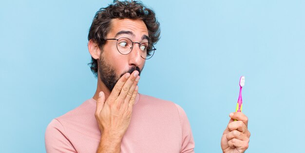 Giovane uomo barbuto che si sente felice, scioccato e sorpreso, coprendo la bocca con la mano e indicando lo spazio laterale della copia