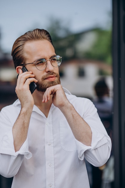 Giovane uomo barbuto che usa il telefono e cammina per strada