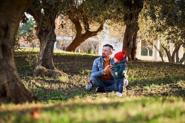 Giovane uomo barbuto felice che gioca con il suo piccolo figlio nel parco