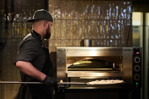 Giovane uomo barbuto in abiti da lavoro che tiene la pizza sul vassoio rotondo