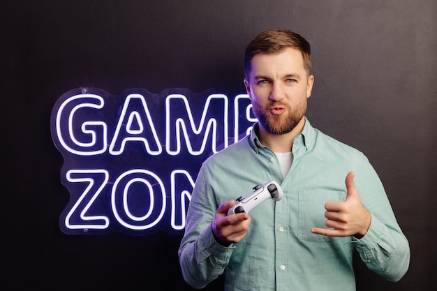 Giovane uomo barbuto in piedi al muro nella stanza e giocare tenendo joystick wireless urlando e vincendo intensa partita di videogioco