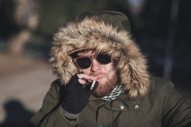 Foto giovane uomo barbuto in un cappuccio di pelliccia sta fumando una sigaretta
