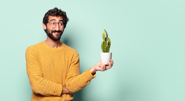 Giovane uomo barbuto pazzo che tiene una pianta della casa del cactus