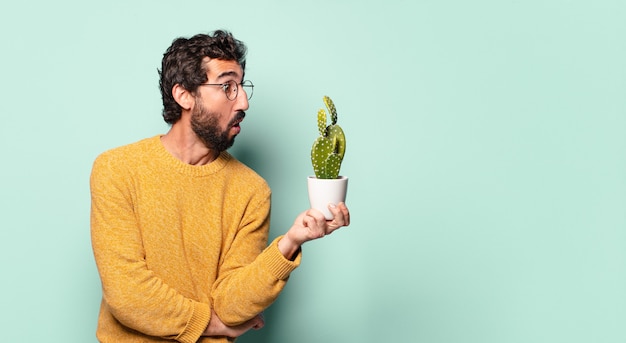 Giovane uomo barbuto pazzo che tiene una pianta della casa del cactus