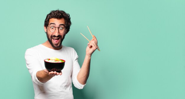 Giovane uomo barbuto pazzo con una ciotola di ramen di noodle