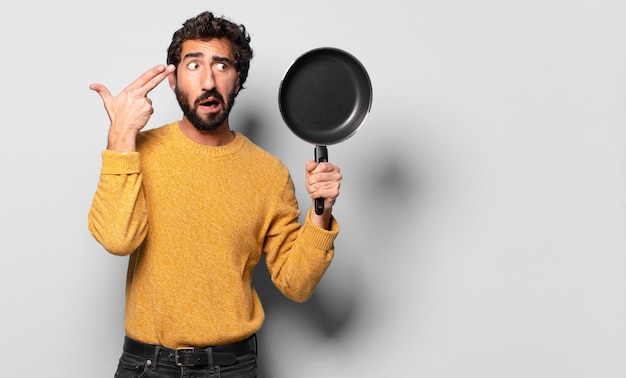 Giovane uomo barbuto pazzo con una padella. concetto di cuoco