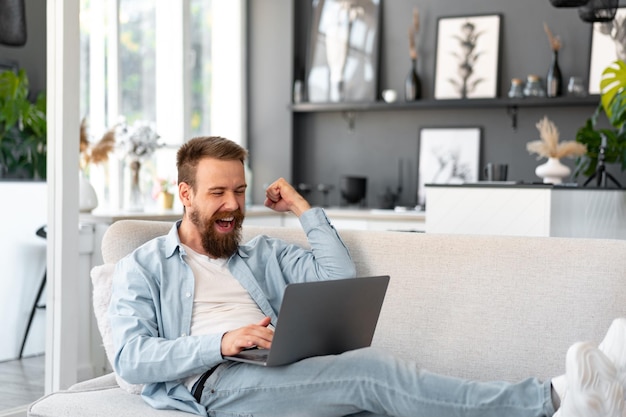 Giovane uomo barbuto seduto sul divano di casa utilizzando il computer portatile