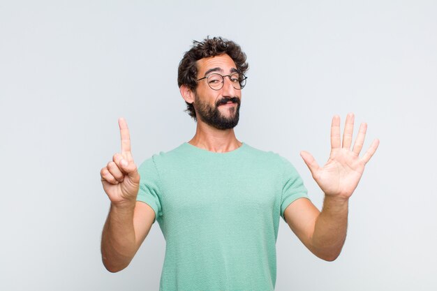 Giovane uomo barbuto sorridente e guardando amichevole, mostrando il numero sei o sesto con la mano in avanti, conto alla rovescia