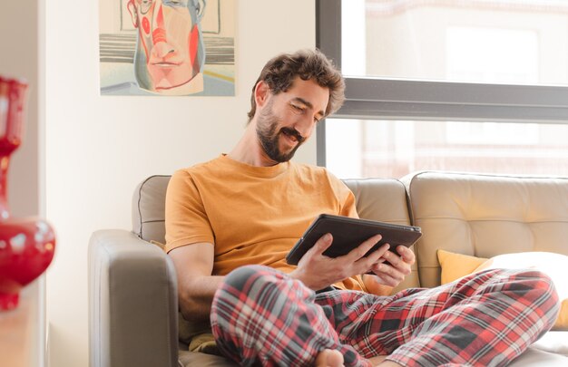 Giovane uomo barbuto su un divano con un tablet touch screen