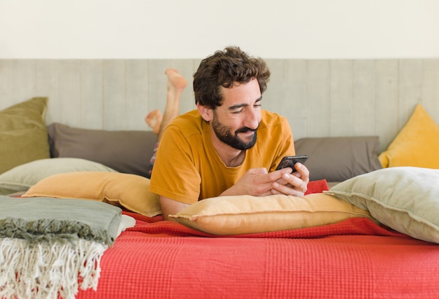 Giovane uomo barbuto su un letto con il suo telefono cellulare