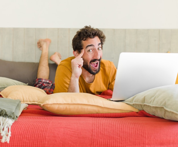 Giovane uomo barbuto su un letto con un computer portatile