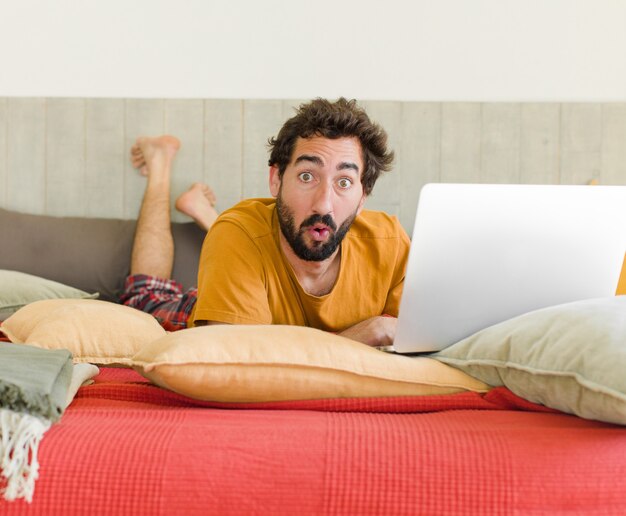 Giovane uomo barbuto su un letto con un laptop