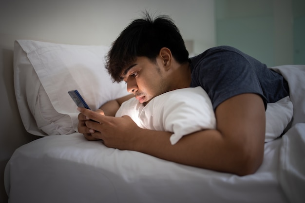 Giovane uomo bello asiatico che utilizza smartphone sul letto