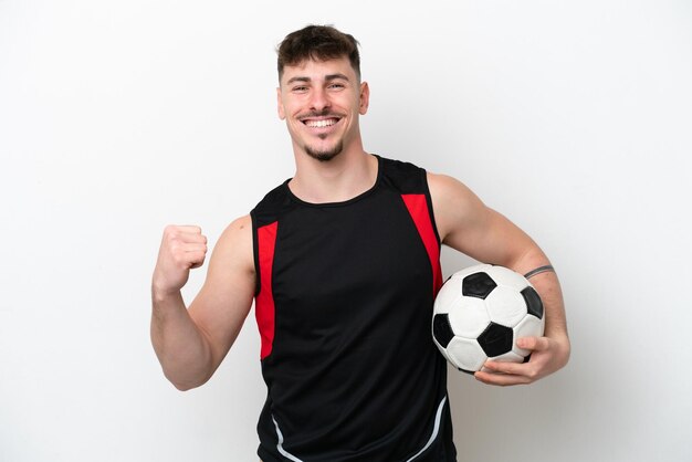 Giovane uomo bello caucasico isolato su sfondo bianco con pallone da calcio che celebra una vittoria