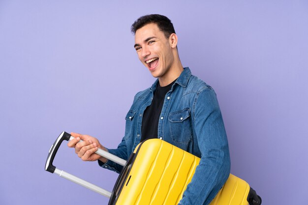 Giovane uomo bello caucasico isolato sulla parete viola in vacanza con la valigia di corsa