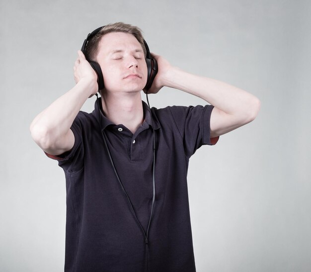 Giovane uomo bello che ascolta musica con le cuffie su sfondo grigio