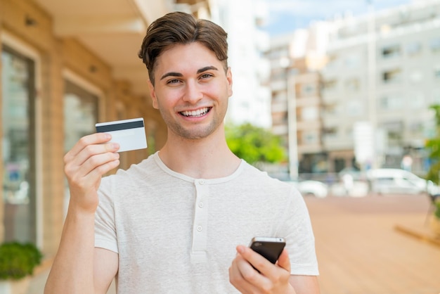 Giovane uomo bello che compra con il cellulare con una carta di credito