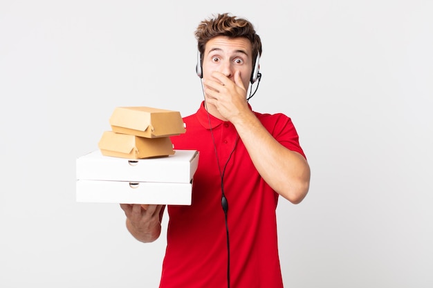 Giovane uomo bello che copre la bocca con le mani con uno scioccato. porta via il concetto di fast food