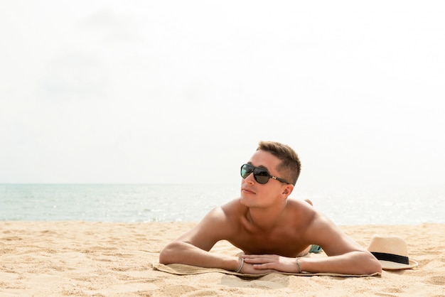 Giovane uomo bello che giace in spiaggia in vacanza d&#39;estate