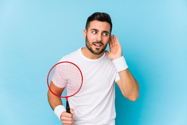 Giovane uomo bello che gioca a badminton isolato cercando di ascoltare un pettegolezzo.