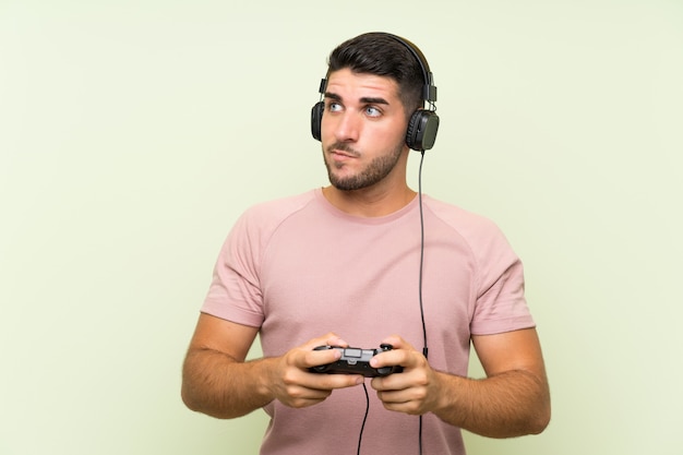 Giovane uomo bello che gioca con un controller di videogioco sopra la parete verde isolata