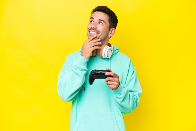 Giovane uomo bello che gioca con un controller di videogioco sul muro isolato guardando in alto mentre sorridente