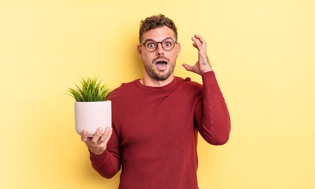 Giovane uomo bello che grida con le mani in alto nel concetto di pianta decorativa dell'aria