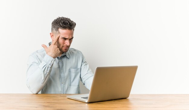 Giovane uomo bello che lavora con il suo computer portatile che mostra un gesto di delusione con l'indice.