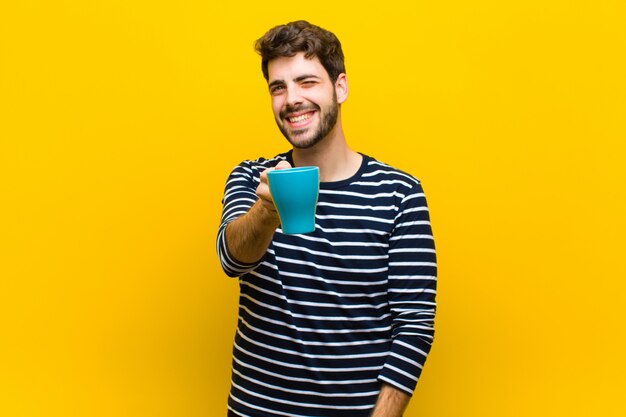 Giovane uomo bello che mangia un caffè contro il fondo arancio