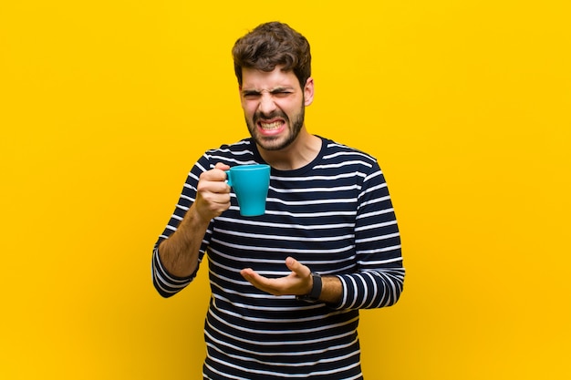 Giovane uomo bello che mangia un caffè contro la parete gialla