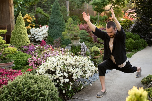 Giovane uomo bello che medita nel giardino dei bonsai