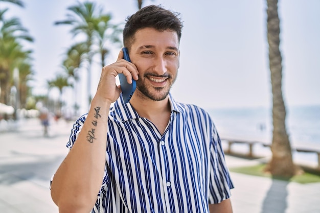 Giovane uomo bello che parla al telefono in riva al mare