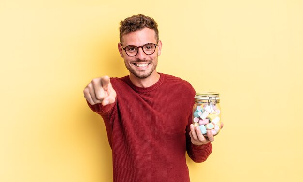 Giovane uomo bello che punta alla telecamera scegliendo te. concetto di caramelle di gelatina