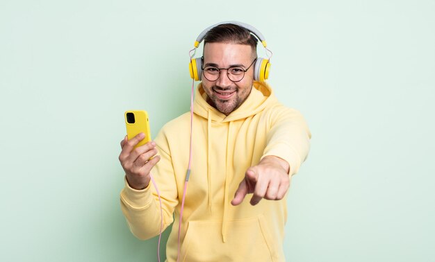 Giovane uomo bello che punta alla telecamera scegliendo te. cuffie e concetto di smartphone