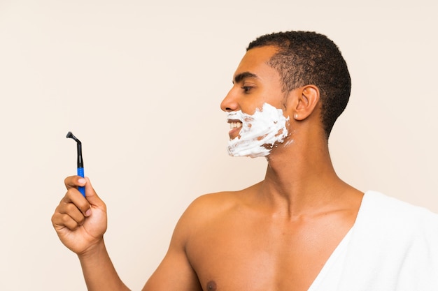 Giovane uomo bello che rade la sua barba sopra la parete isolata con l'espressione felice