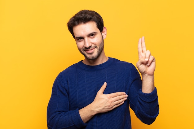 Giovane uomo bello che sembra felice, fiducioso e degno di fiducia, sorridente e mostrando segno di vittoria, con un atteggiamento positivo