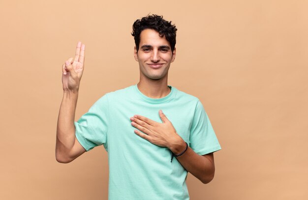 Giovane uomo bello che sembra felice, fiducioso e degno di fiducia, sorridente e mostrando segno di vittoria, con un atteggiamento positivo