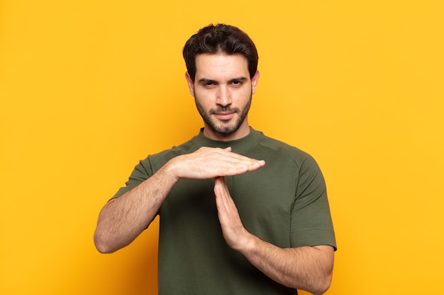 giovane uomo bello che sembra serio, severo, arrabbiato e dispiaciuto, facendo segno di time out